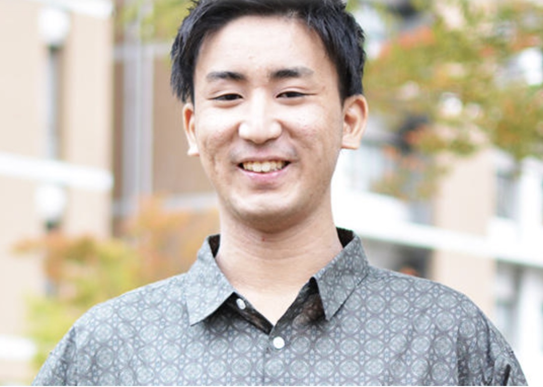 薗部健太さん。木々を背にシャツ姿で笑っている